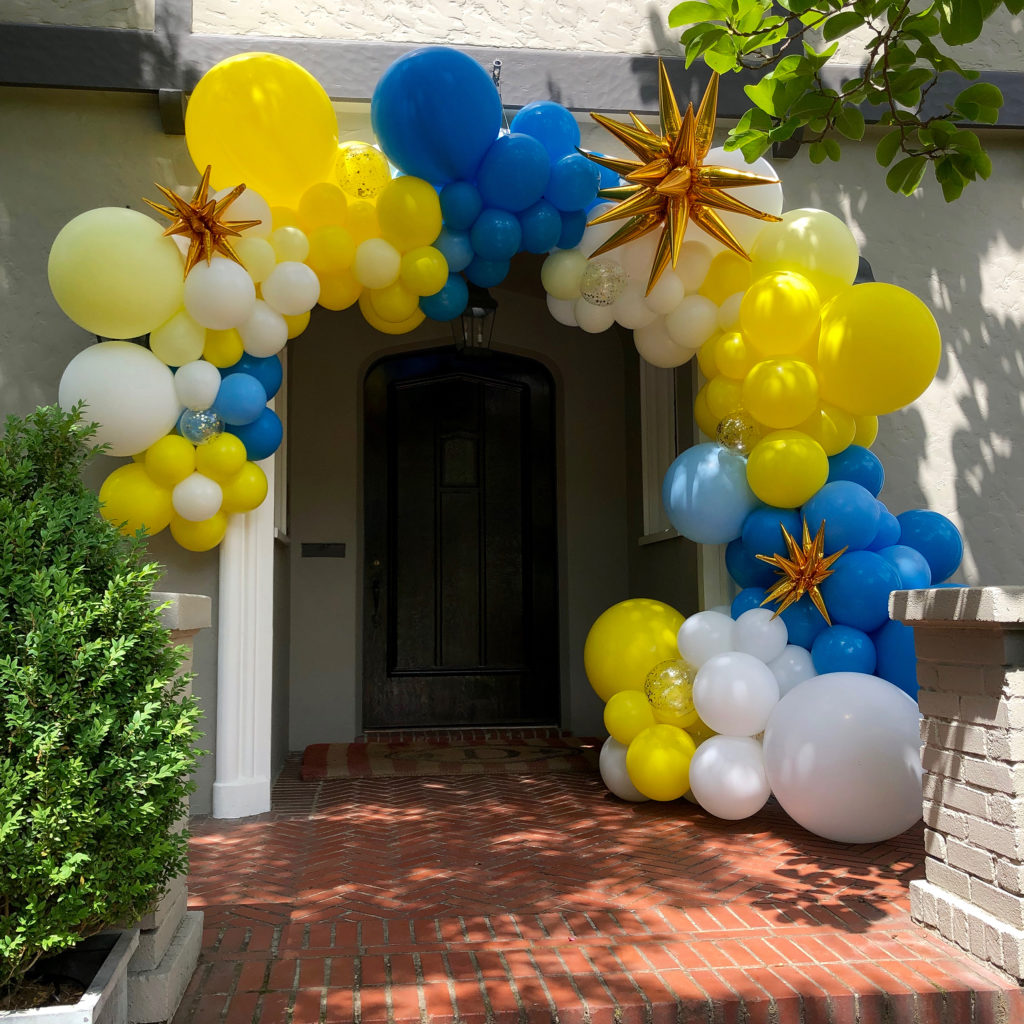 Organic Style Garland with yellow, blue, and white balloons, decorated with gold starbursts and confetti balloons, is hung over a recessed doorway.