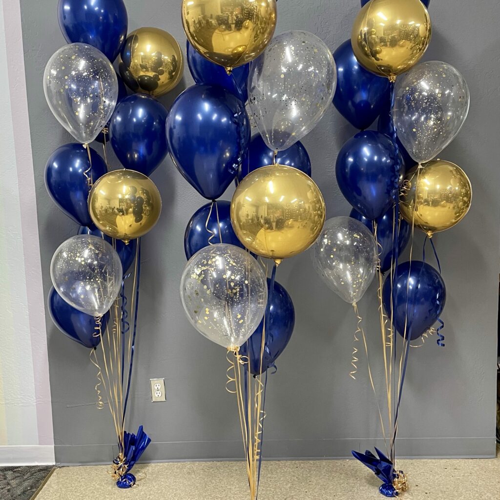 Three 10-Balloon Spray with 6 Sapphire Blue balloons, 2 clear balloons with Gold Confetti, and 2 Gold Orbz are secured with matching blue weights and lined up against a grey wall. A classy way to highlight any space.